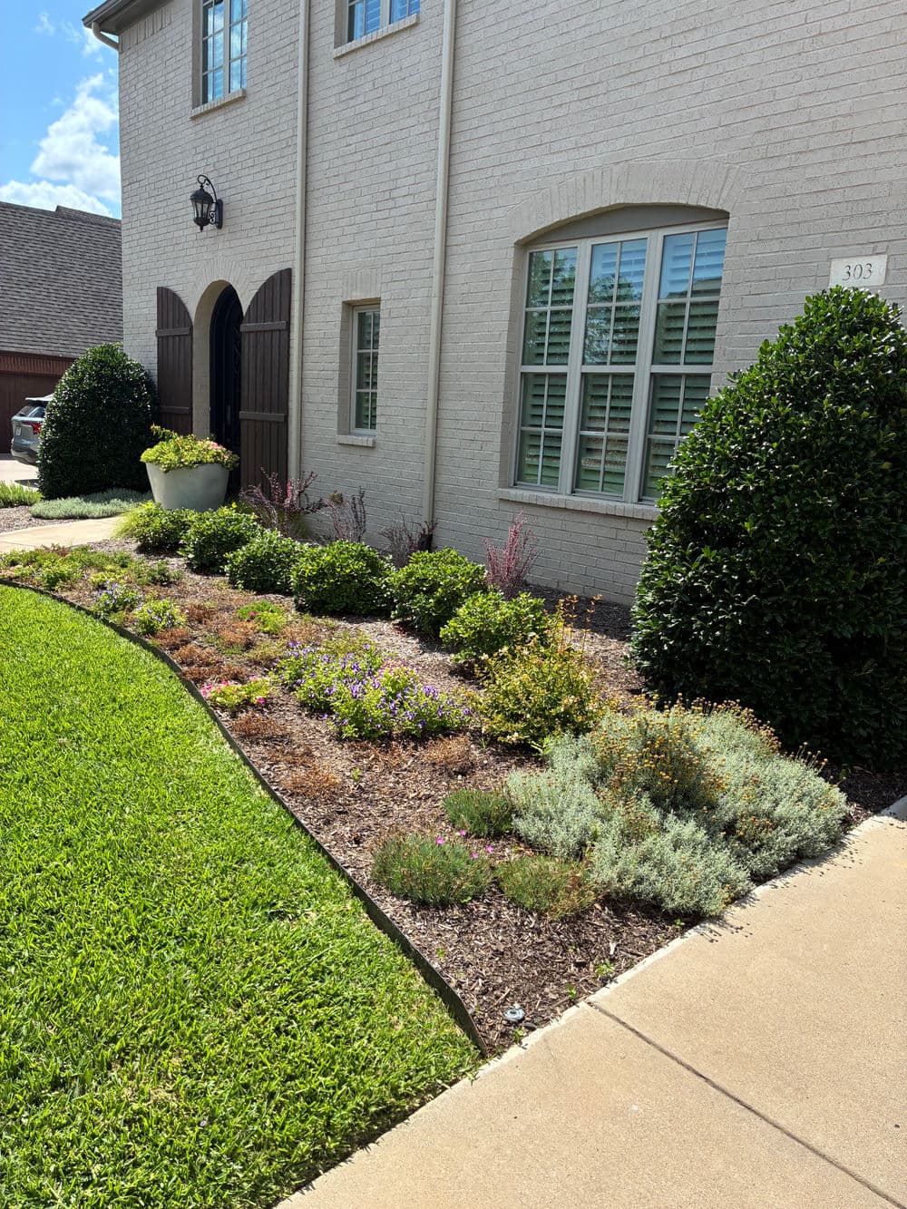 Lush front yard landscaping with colorful flowers and manicured shrubs by a brick house.