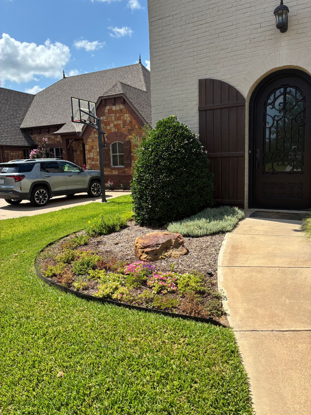 Front yard landscaping with bushes, flowers, and a decorative stone near a home's entrance.