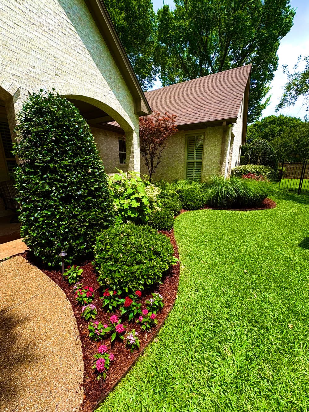 Lush garden with blooming flowers, well-manicured shrubs, and vibrant green lawn beside a house.