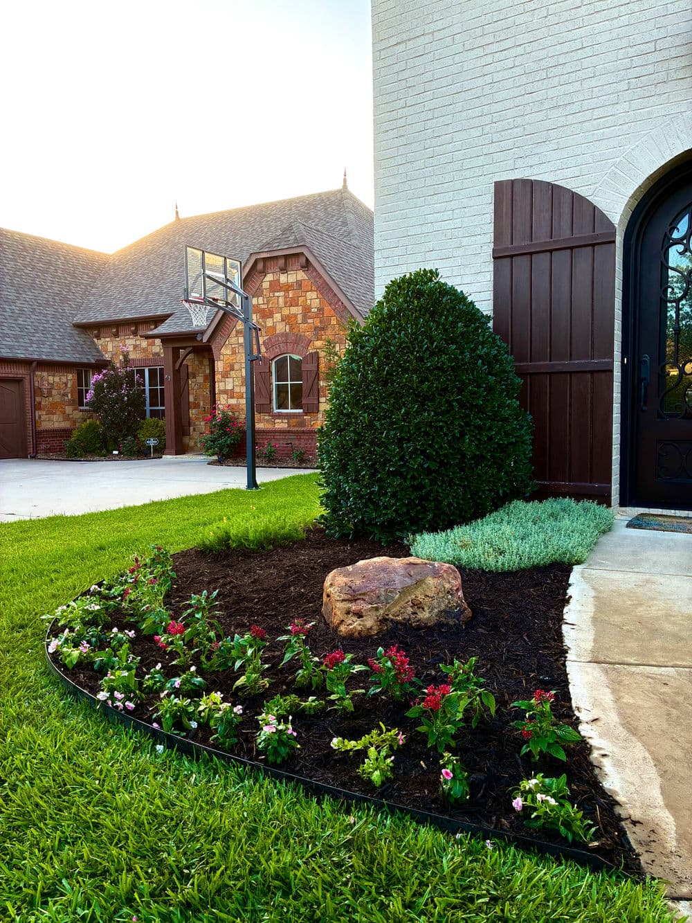 Lush garden with colorful flowers, neatly arranged stones, and a basketball hoop beside a home.