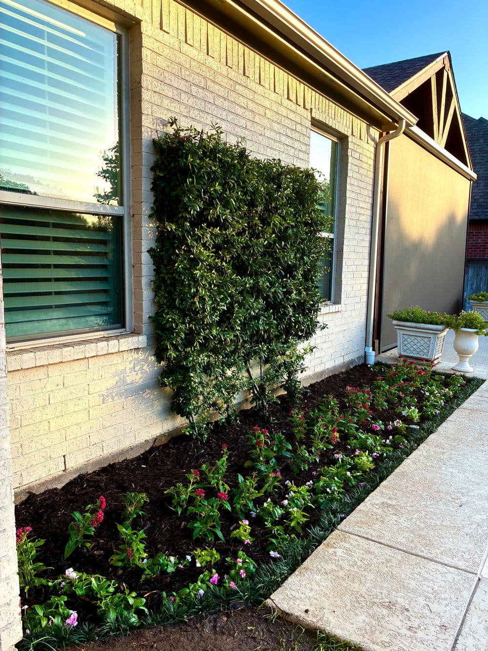 Well-maintained garden with colorful flowers and lush greenery beside a brick house facade.