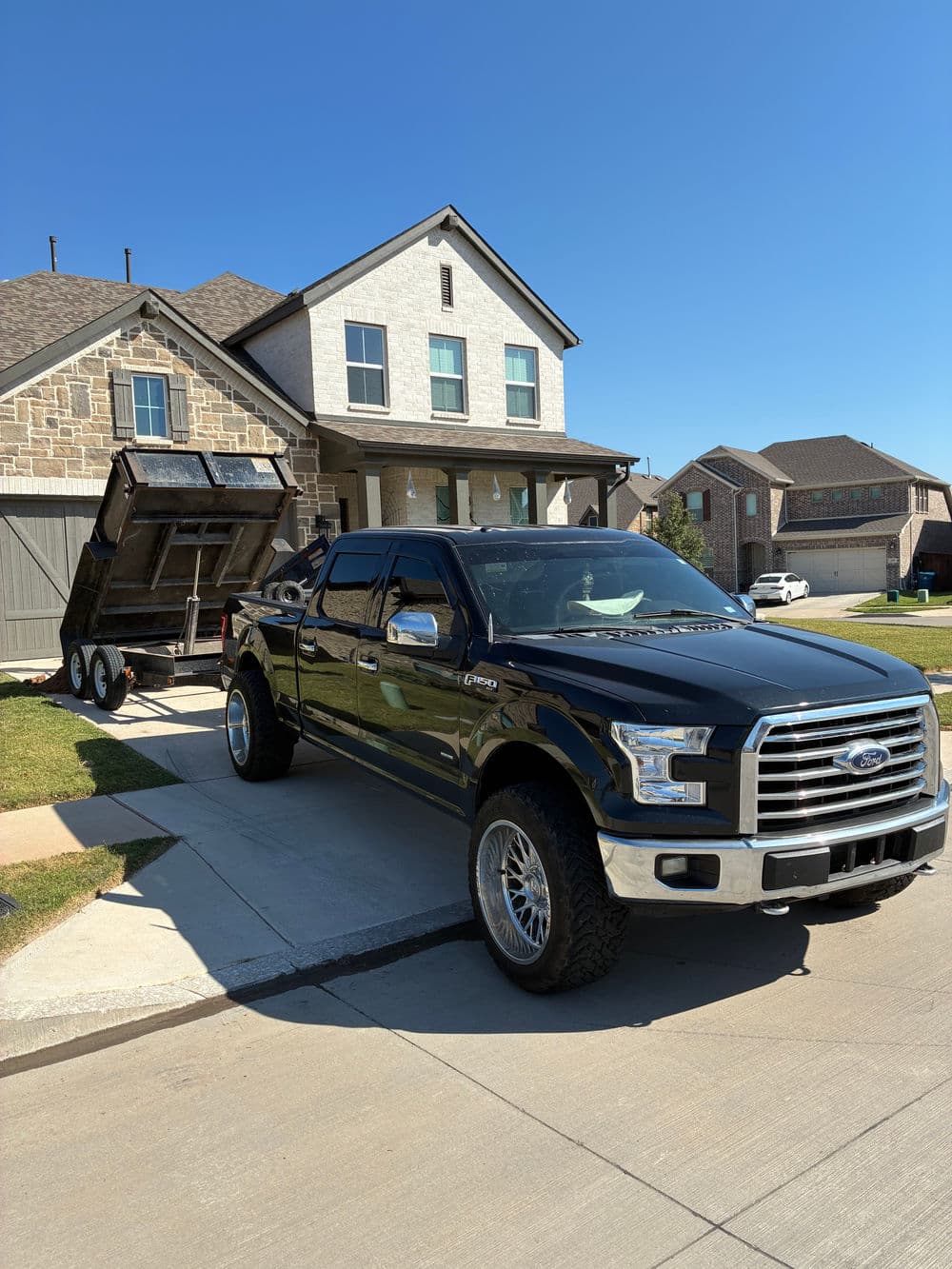 Black Ford F-150 truck parked in driveway with a trailer in front of a modern house.