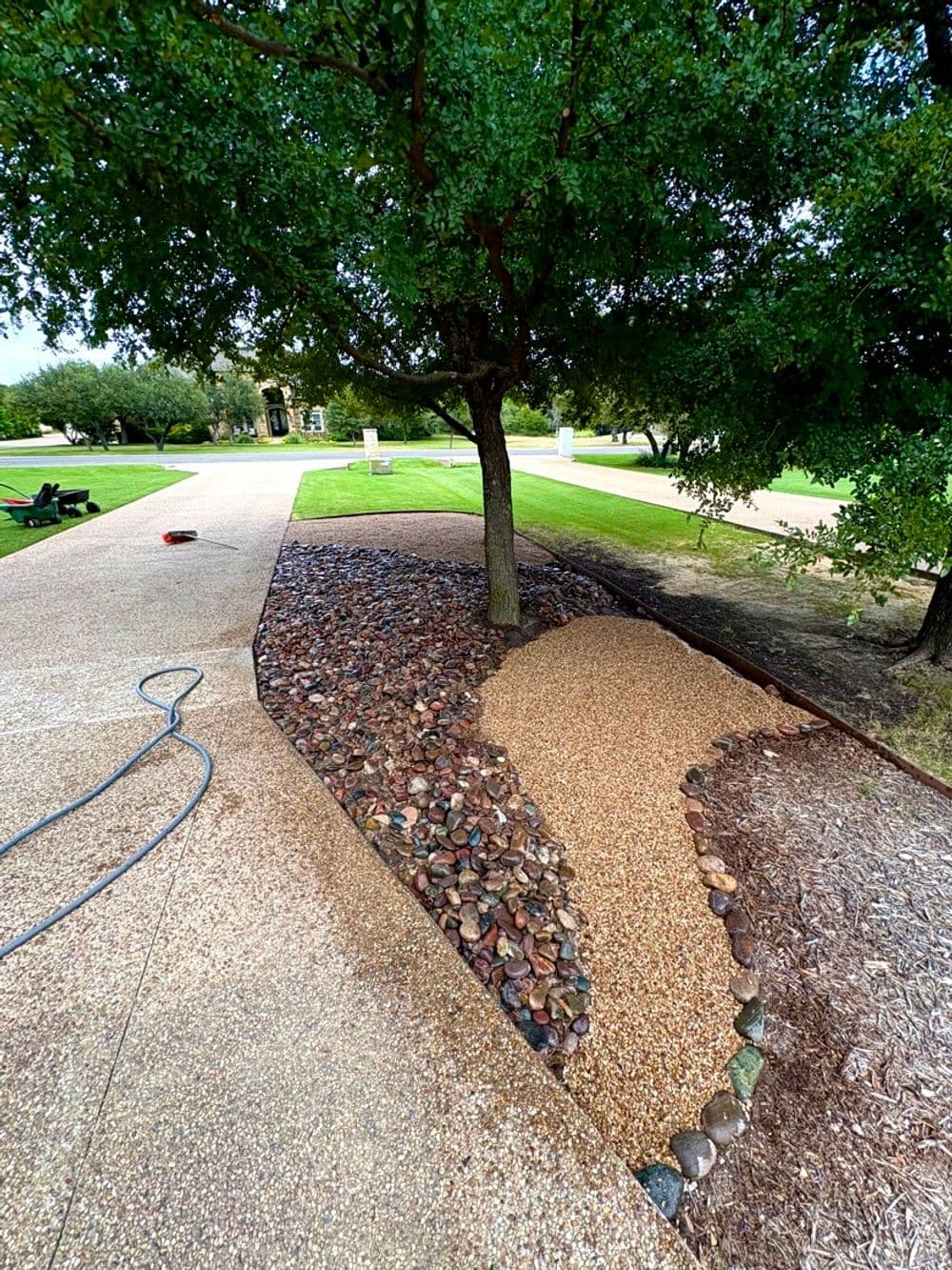 Landscape design featuring gravel and stone pathway under a tree in a manicured yard.