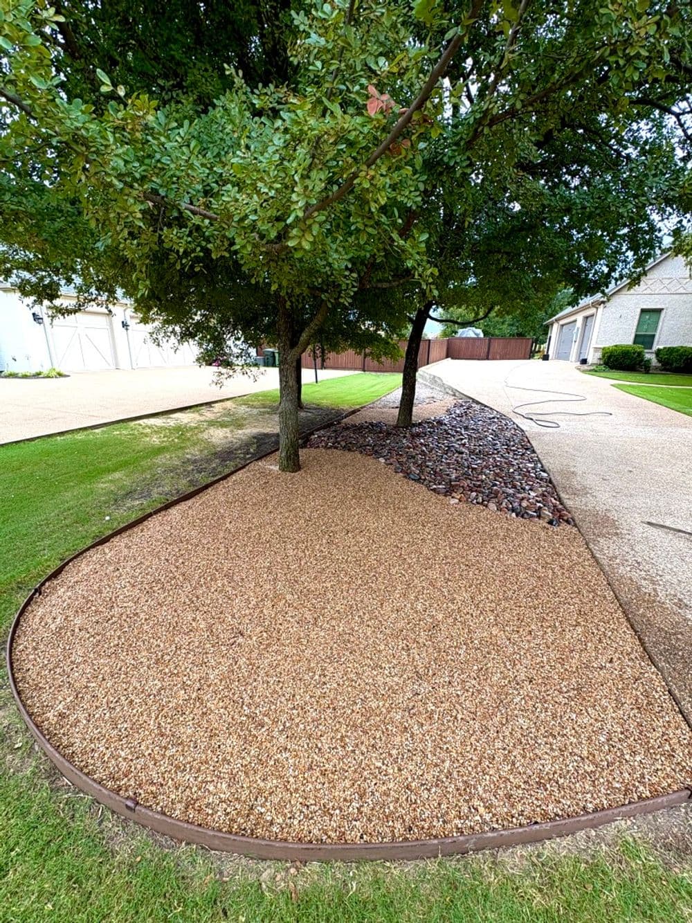 Landscaped garden area with gravel and stones under trees, featuring neat edging.