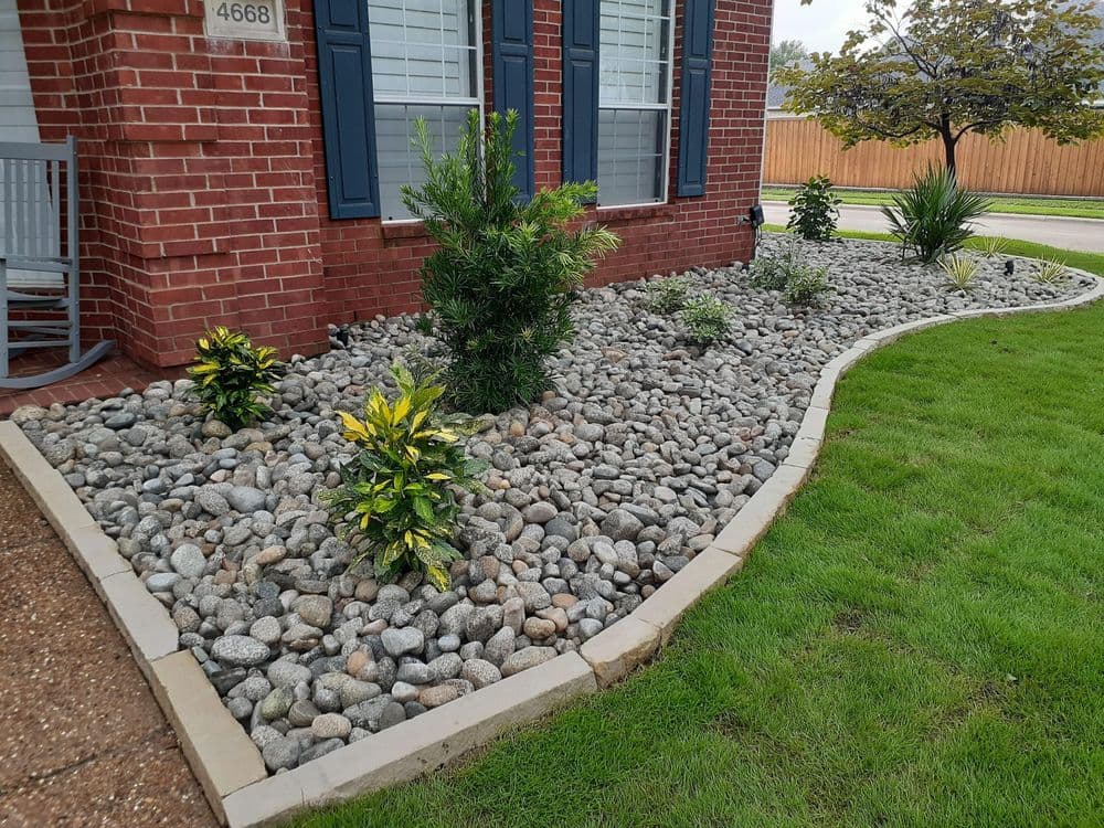 Landscaped garden with decorative rocks, plants, and trimmed grass near a brick home.