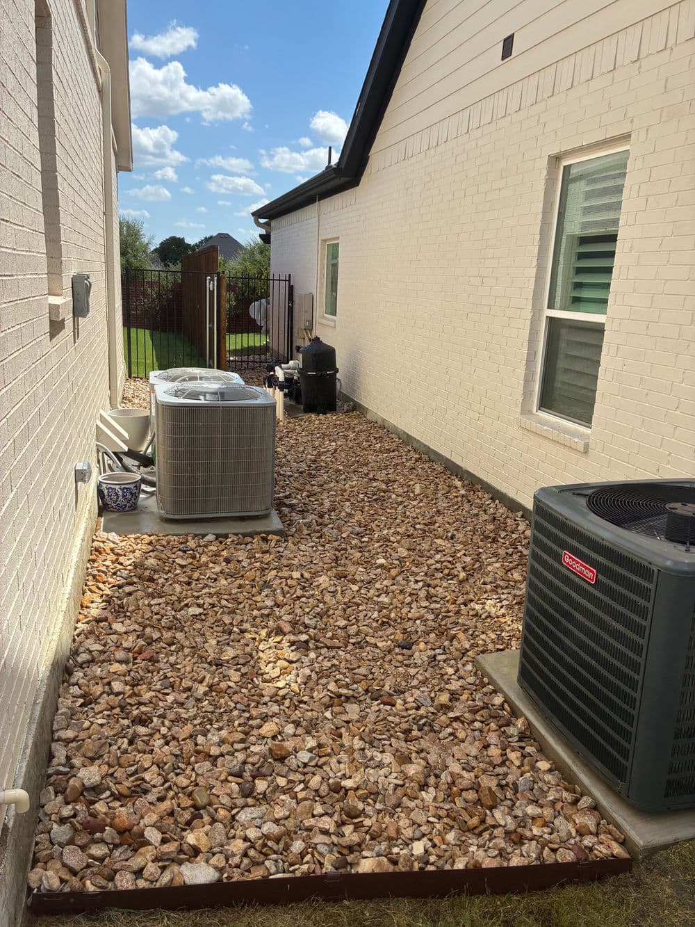 Side yard with decorative rocks, air conditioning units, and sunny blue sky.
