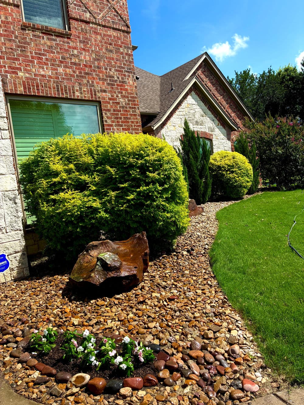 Lush landscaping with shrubs, rocks, and flowers adorning a brick home exterior.