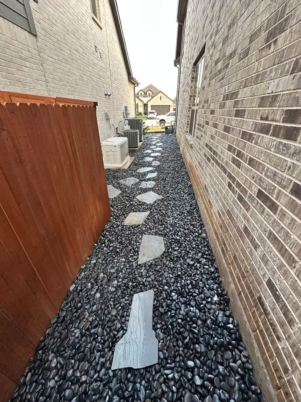 Pathway of slate stepping stones on gravel beside residential buildings.
