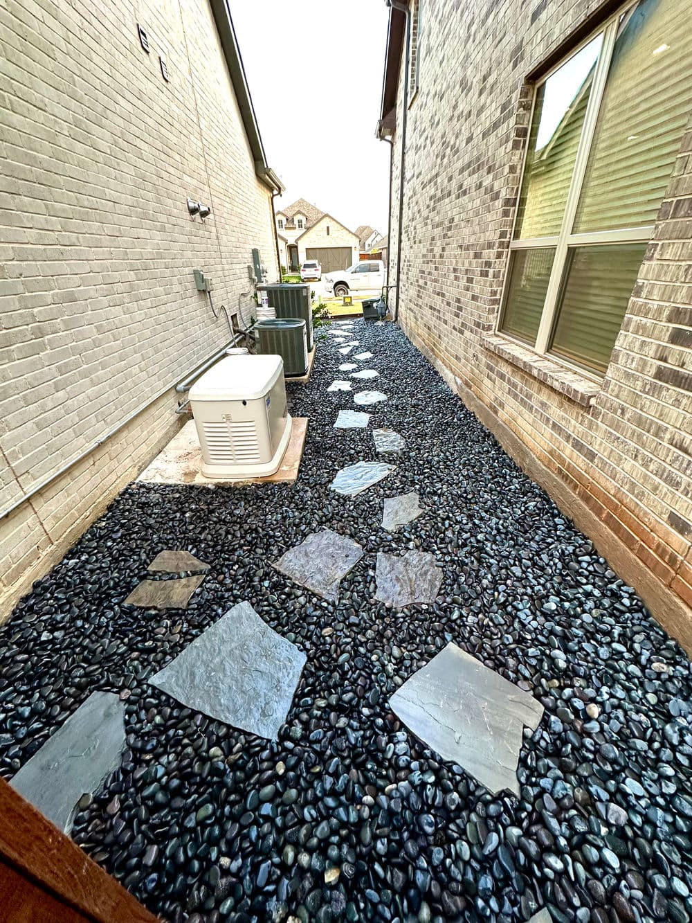 Side yard pathway with slate stones and black pebbles between two houses.