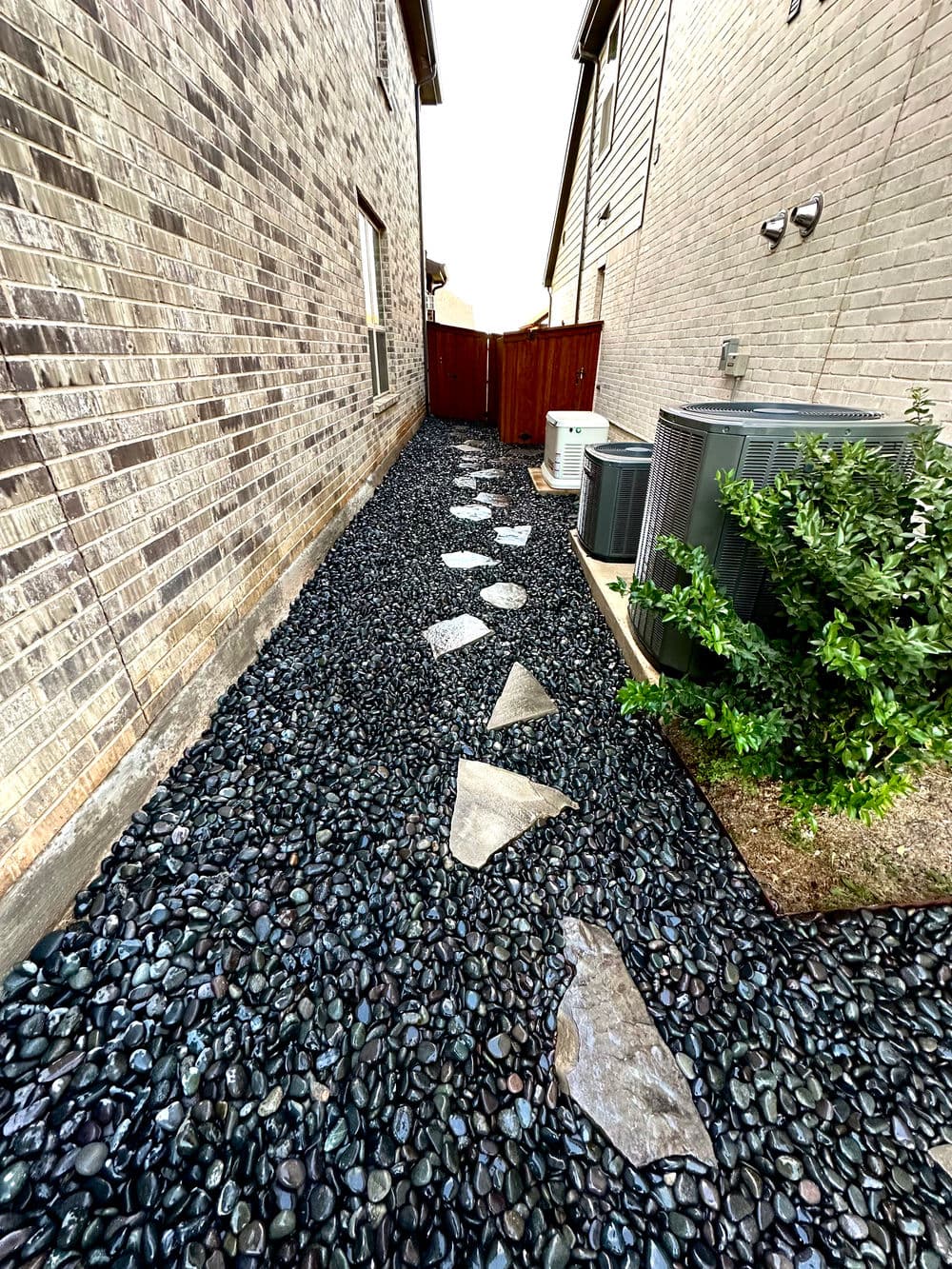 Garden pathway made of stones on black pebbles between two houses, showcasing landscape design.