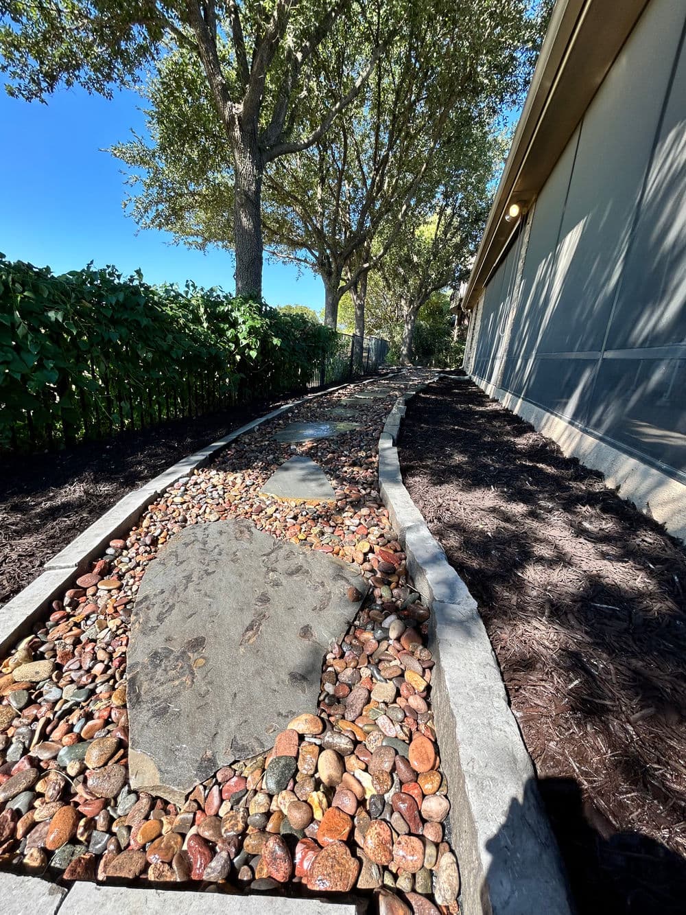 Landscaped stone pathway lined with trees and mulch, leading beside a home.
