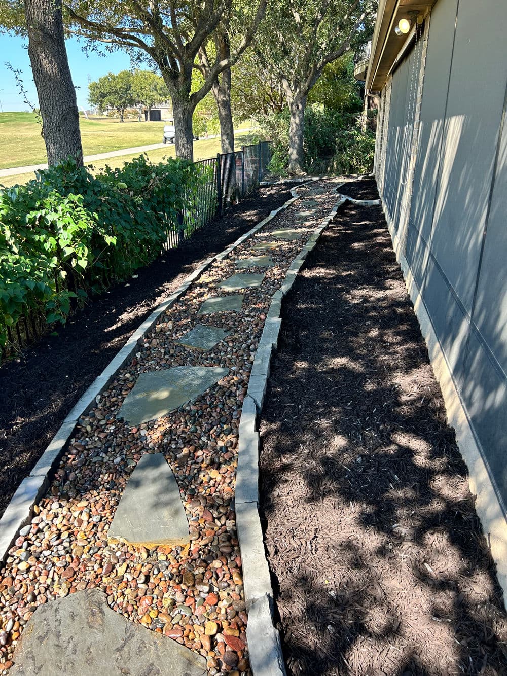 Decorative garden pathway with stone and pebbles alongside a house, surrounded by trees.