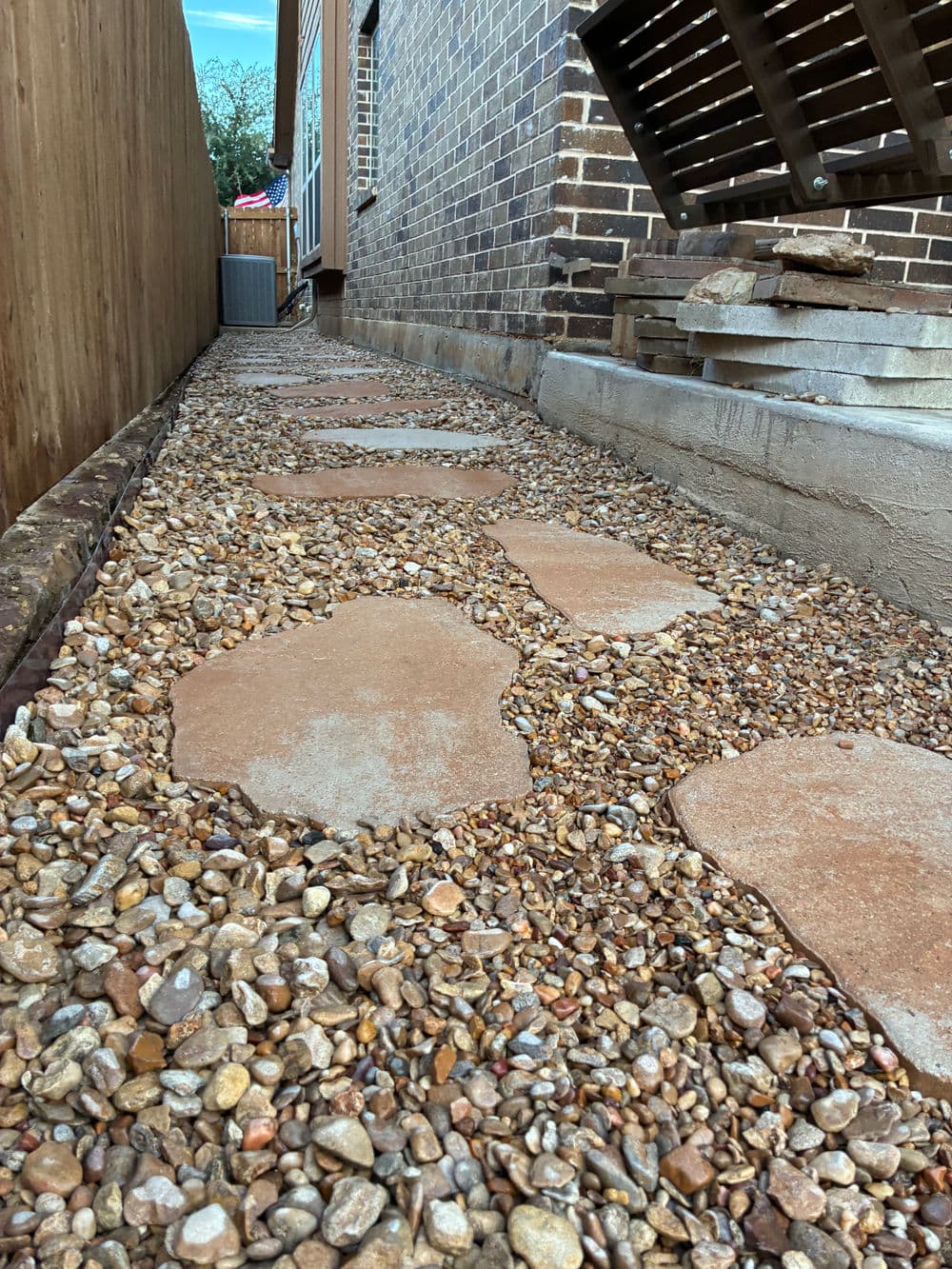 Paver stone walkway through gravel pathway beside a brick house.