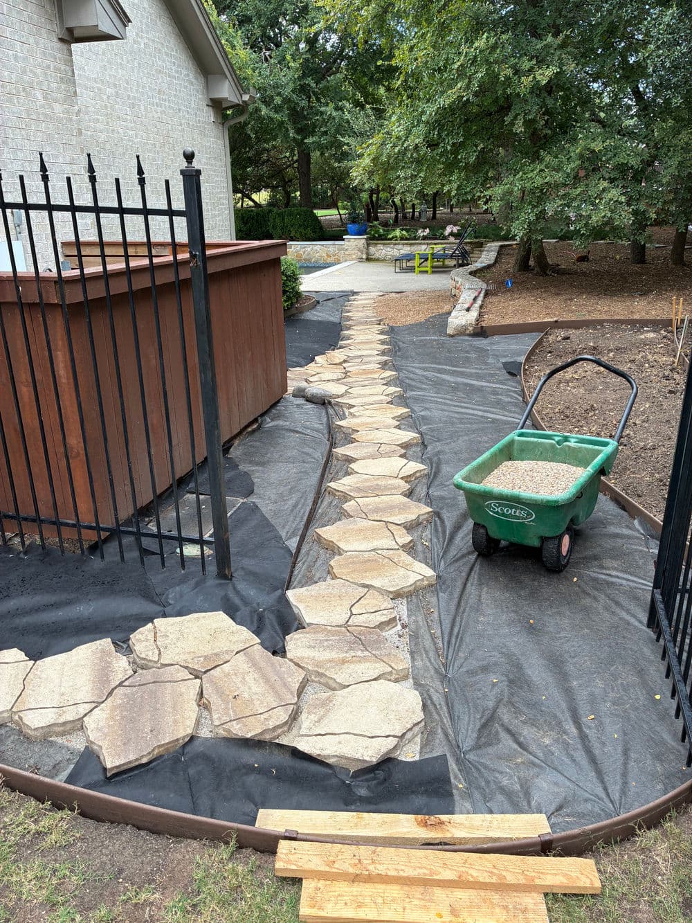 Pathway of stone pavers surrounded by landscaping fabric and a wheeled cart in a garden.