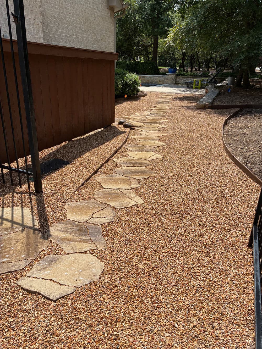 Stone pathway with gravel landscaping leading to a garden area beside a house.