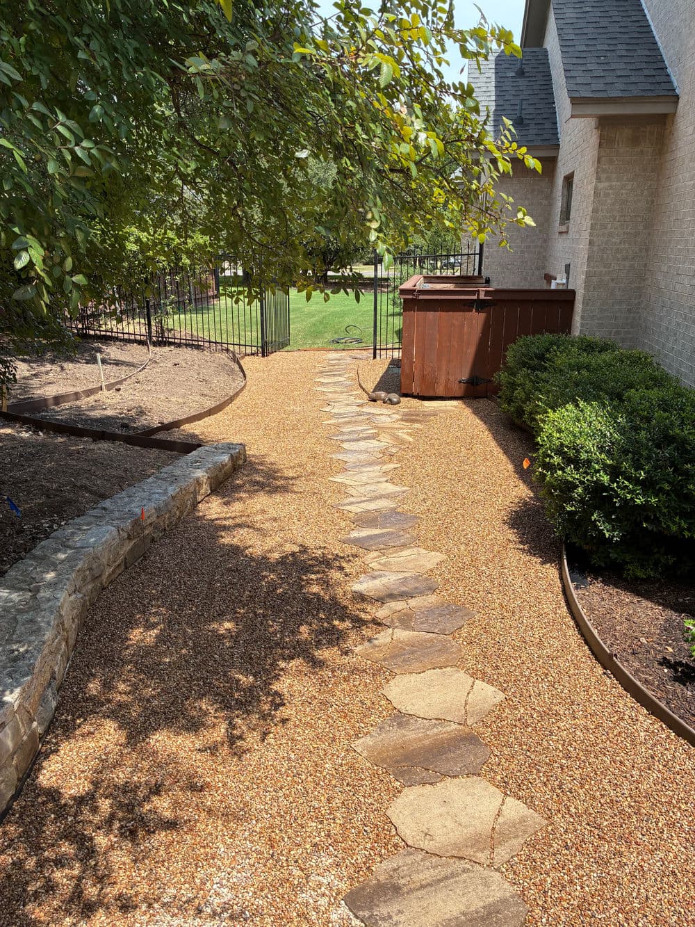 Pathway featuring stone stepping stones and gravel, surrounded by lush landscaping and a gate.