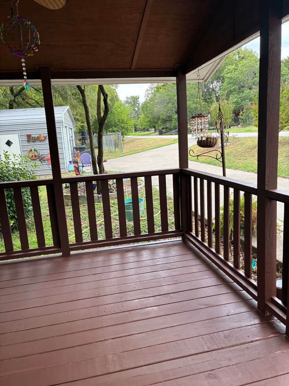 View of a brown wooden porch with plants and a road in the background on a sunny day.