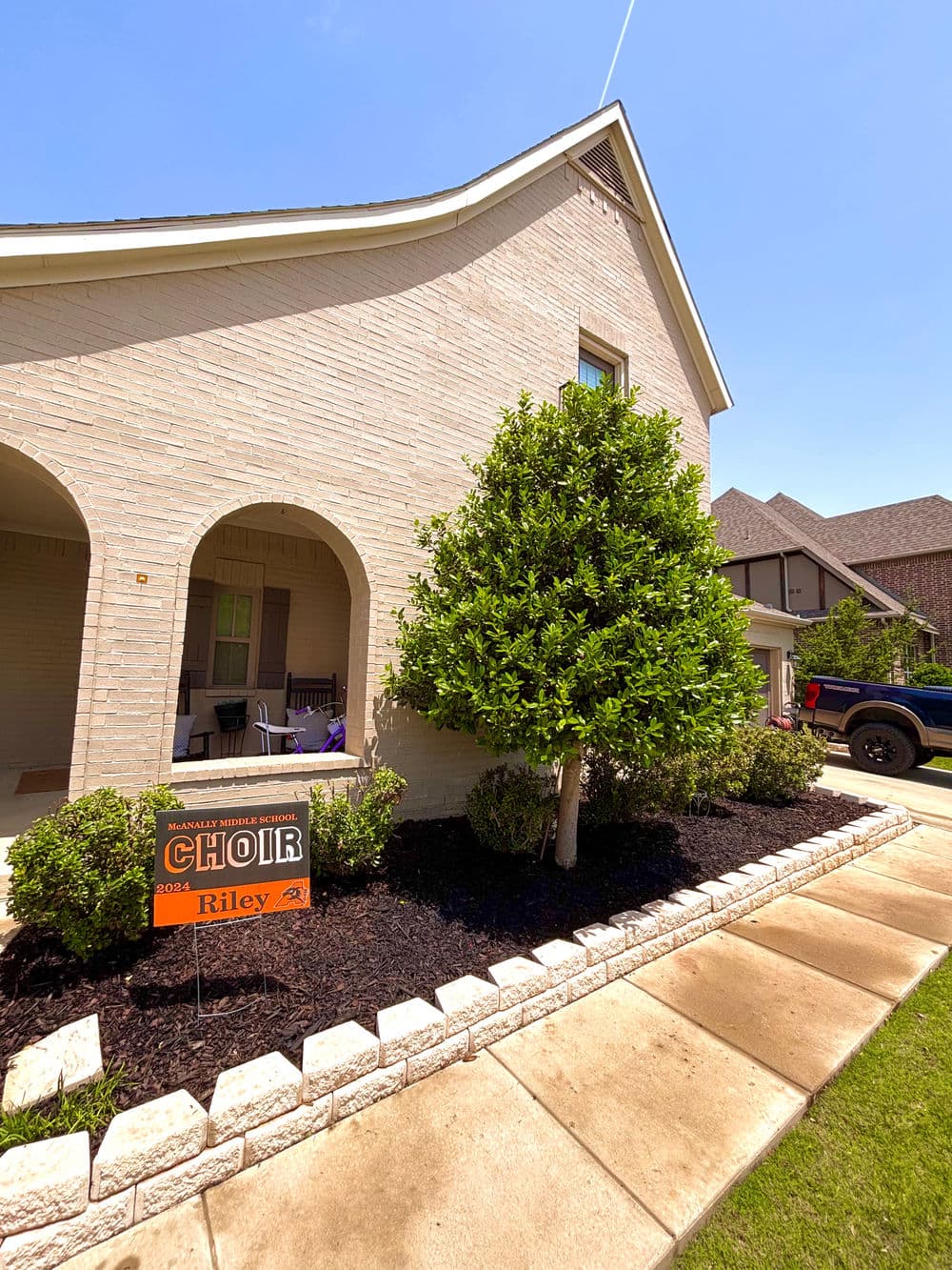 House exterior featuring a choir sign for Riley, lush greenery, and a clear blue sky.